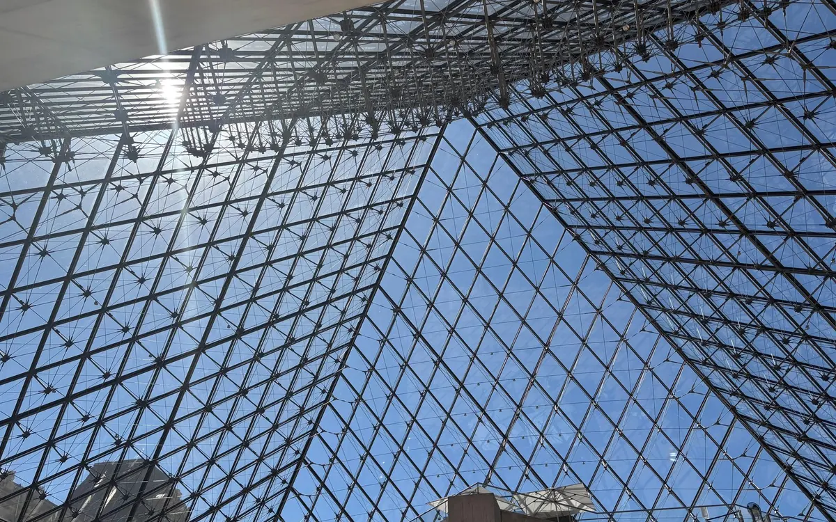 The glass and steel grid of the Louvre pyramid seen from below in the courtyard