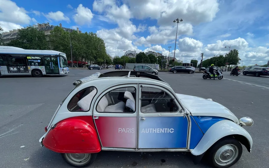 A red, white and blue 2CV parked on a wide Paris square