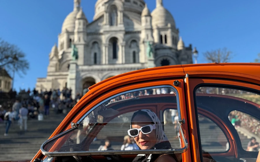 A red vintage convertible below the Sacré-Cœur, a passenger in sunglasses at the wheel