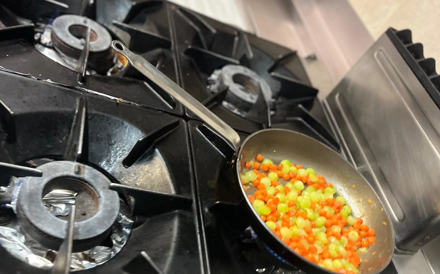 Diced vegetables in a pan on a gas stove in the kitchen