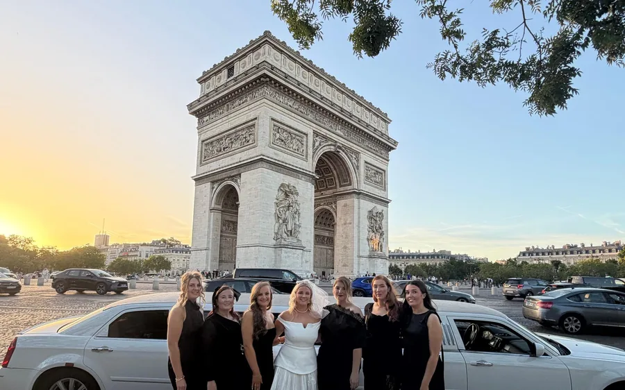 A group in black beside a white limousine at the Arc de Triomphe at sunset