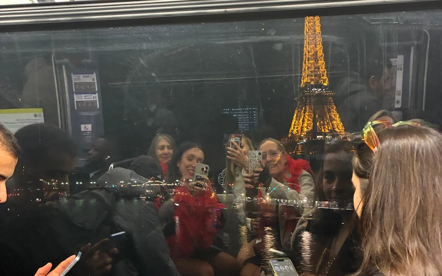 Passengers on a bus at night with the Eiffel Tower reflected in the window