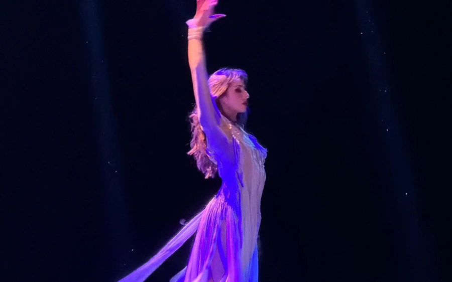 A dancer in a feathered costume on stage under purple light