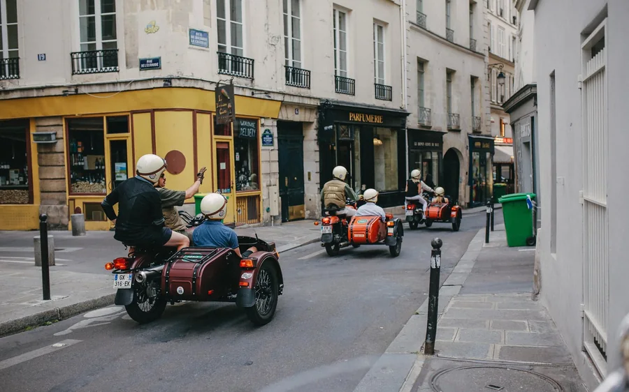Vintage motorcycle sidecars with helmeted passengers on a narrow street