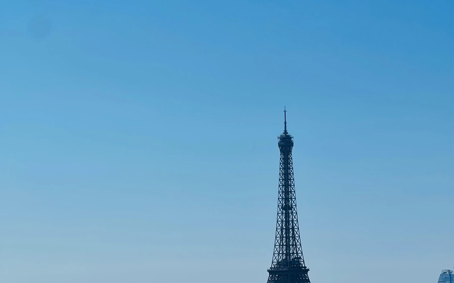 The upper half of the Eiffel Tower seen from across the city under a clear sky