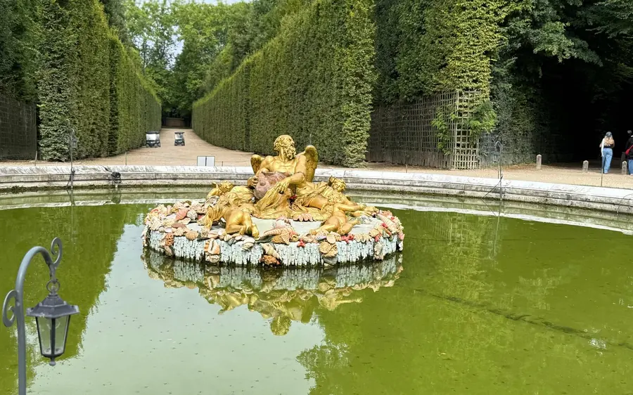 A gilded fountain in a green basin in the gardens of Versailles