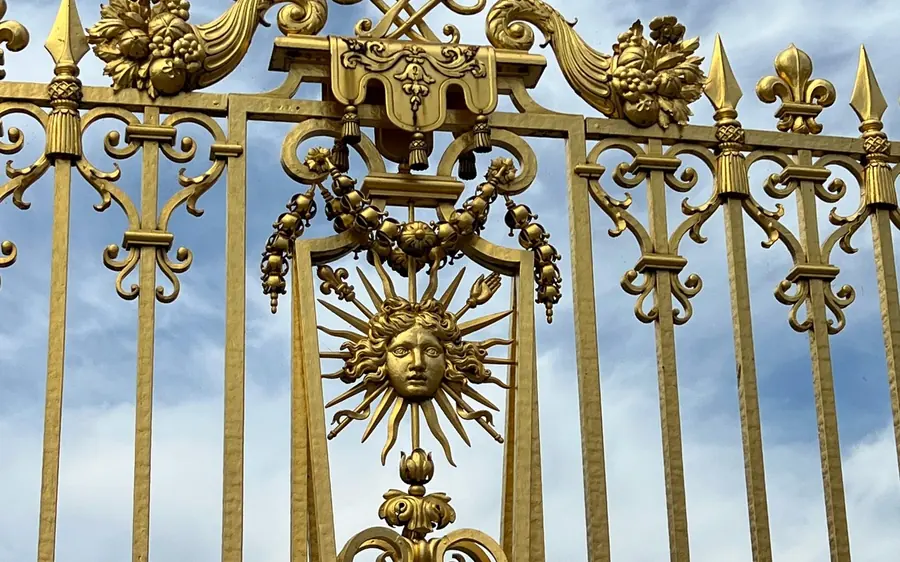 The gilded gate of the Palace of Versailles with its sun emblem